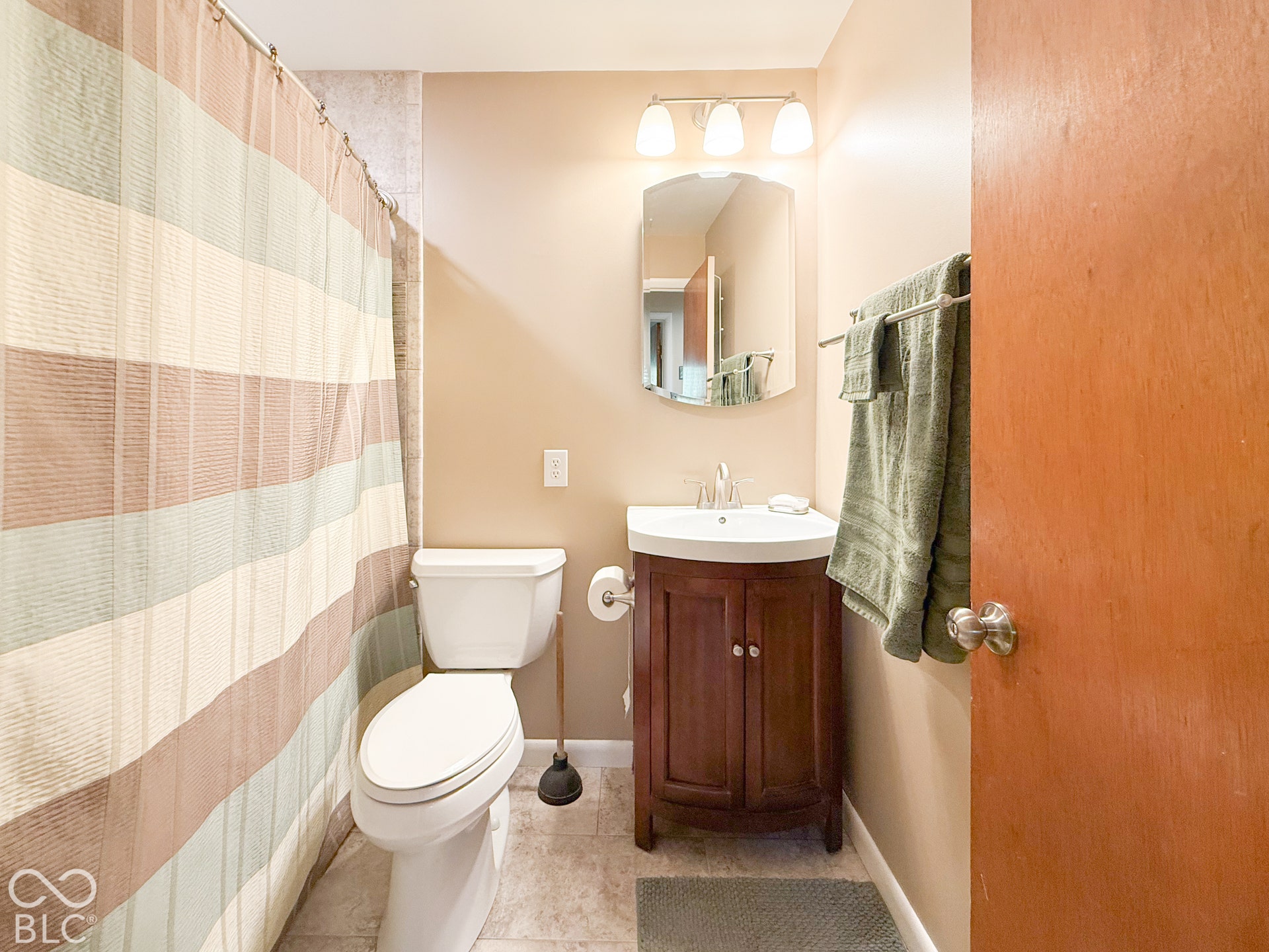 4225 Westbourne Drive, Indianapolis, IN 46205 Bathroom featuring a curved dark wood vanity with a white basin, a polished chrome single-lever faucet, a decorative wall-mounted mirror, and a three-light fixture