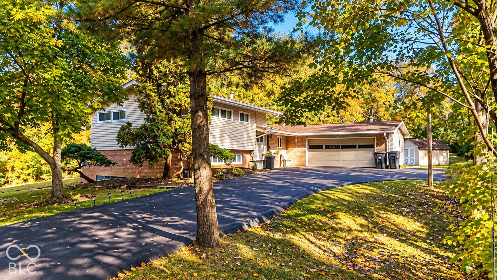 4225 Westbourne Drive, Indianapolis, IN 46205 Split-level exterior featuring a brick and horizontal siding facade, attached two-car garage, asphalt driveway, and mature landscaping