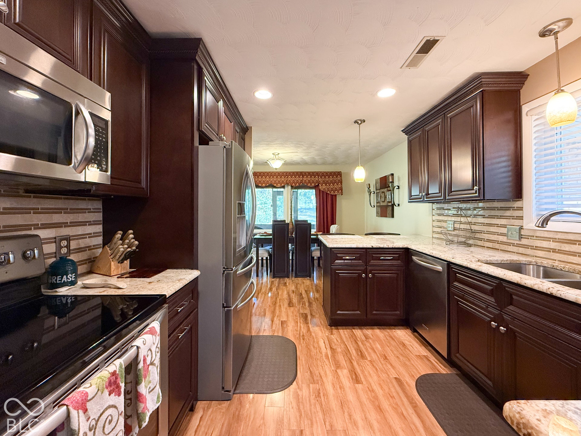 4225 Westbourne Drive, Indianapolis, IN 46205 Kitchen featuring stained wood cabinetry, light-toned stone countertops, stainless steel appliances, horizontally-tiled backsplash, and wood-finish flooring