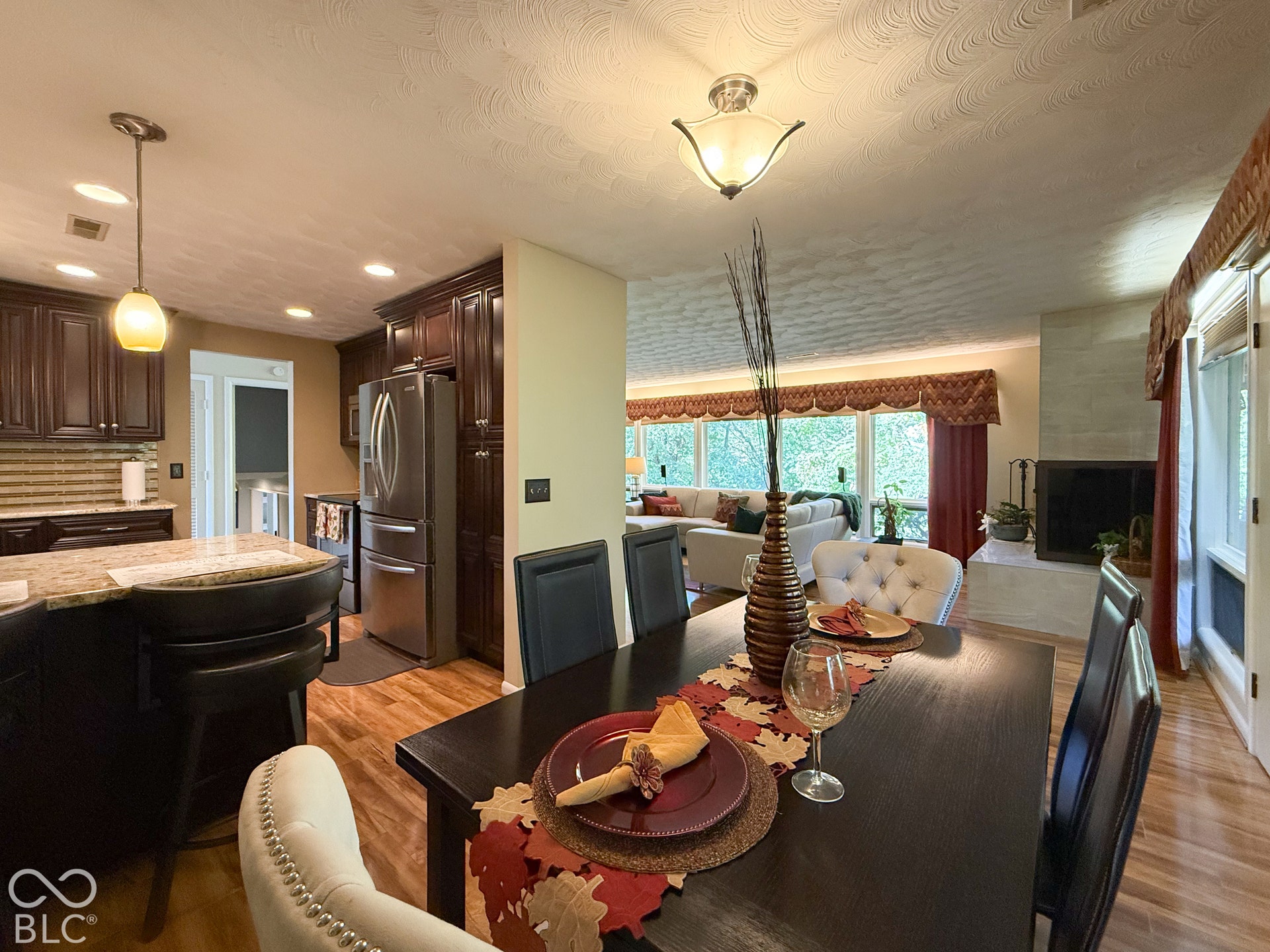 4225 Westbourne Drive, Indianapolis, IN 46205 Kitchen featuring dark wood cabinetry, stone countertops, stainless steel appliances, wood-finish flooring, and a fireplace with a light-toned stone surround