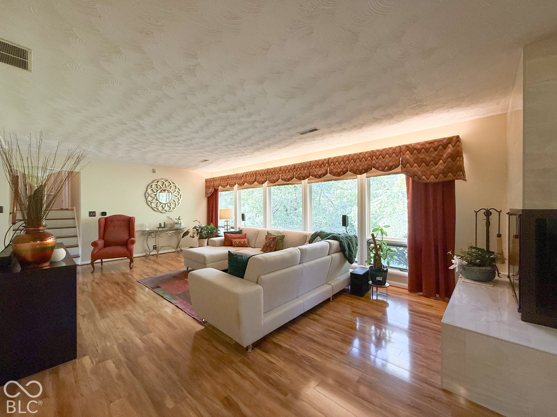 4225 Westbourne Drive, Indianapolis, IN 46205 Living area featuring polished wood-finish flooring, a wall of expansive windows, and a hearth with a stone-surround fireplace
