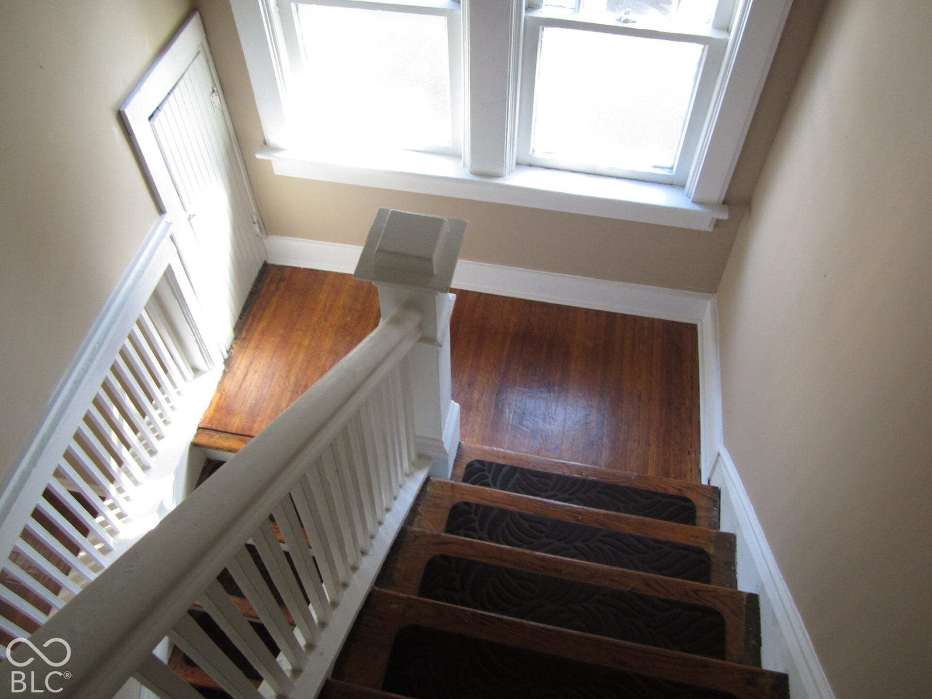 Staircase featuring wood-finish treads, a white wooden balustrade with a square newel post, polished wood-finish flooring, and a built-in cabinet