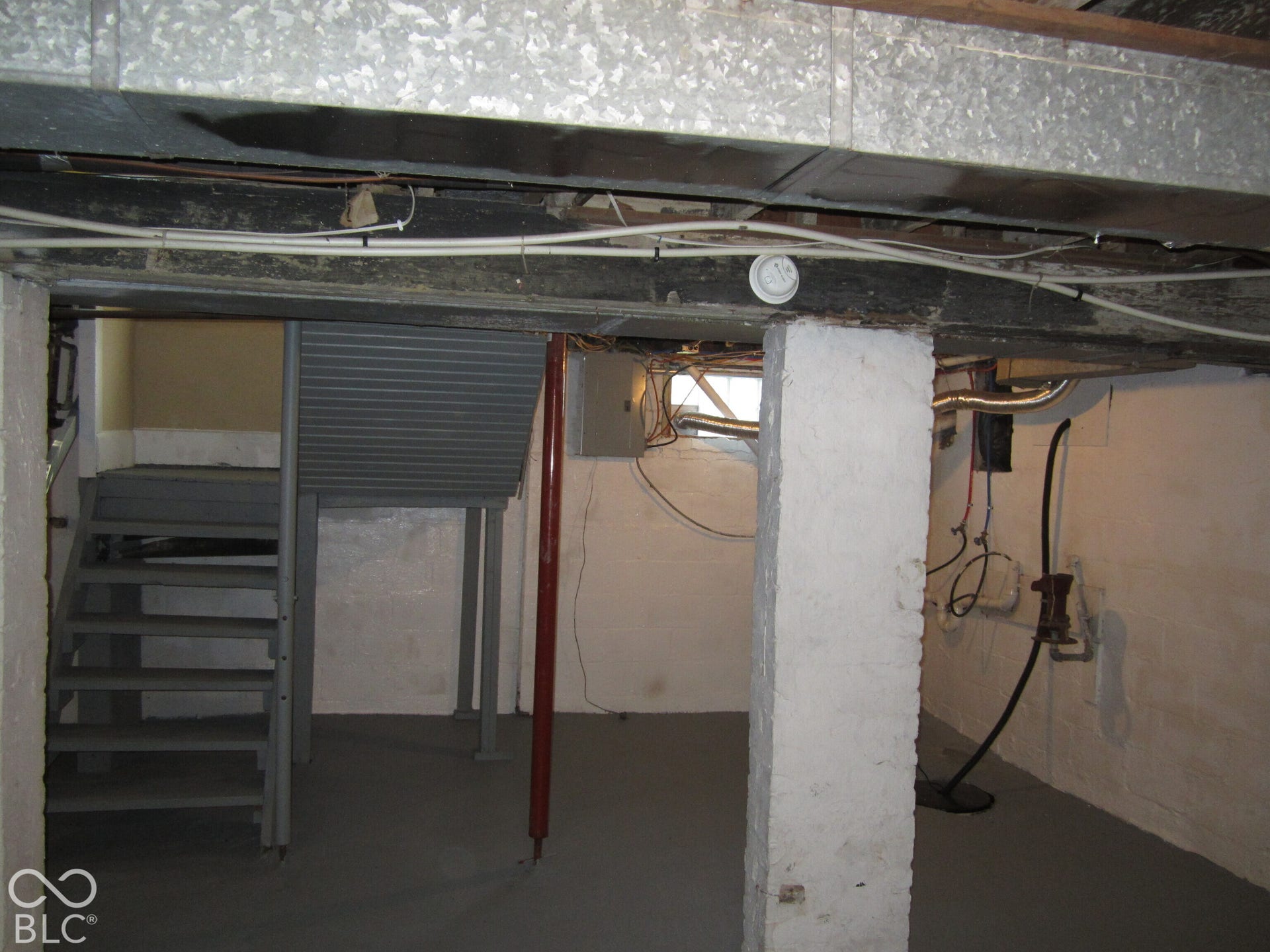 Unfinished basement area featuring painted masonry walls, concrete flooring, structural support column, and open staircase
