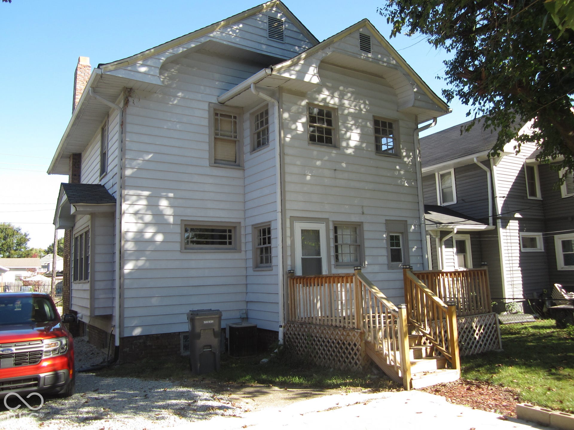 Two-story residential exterior featuring horizontal siding, decorative gable brackets, multiple multi-pane windows, and a raised wooden deck with lattice skirting