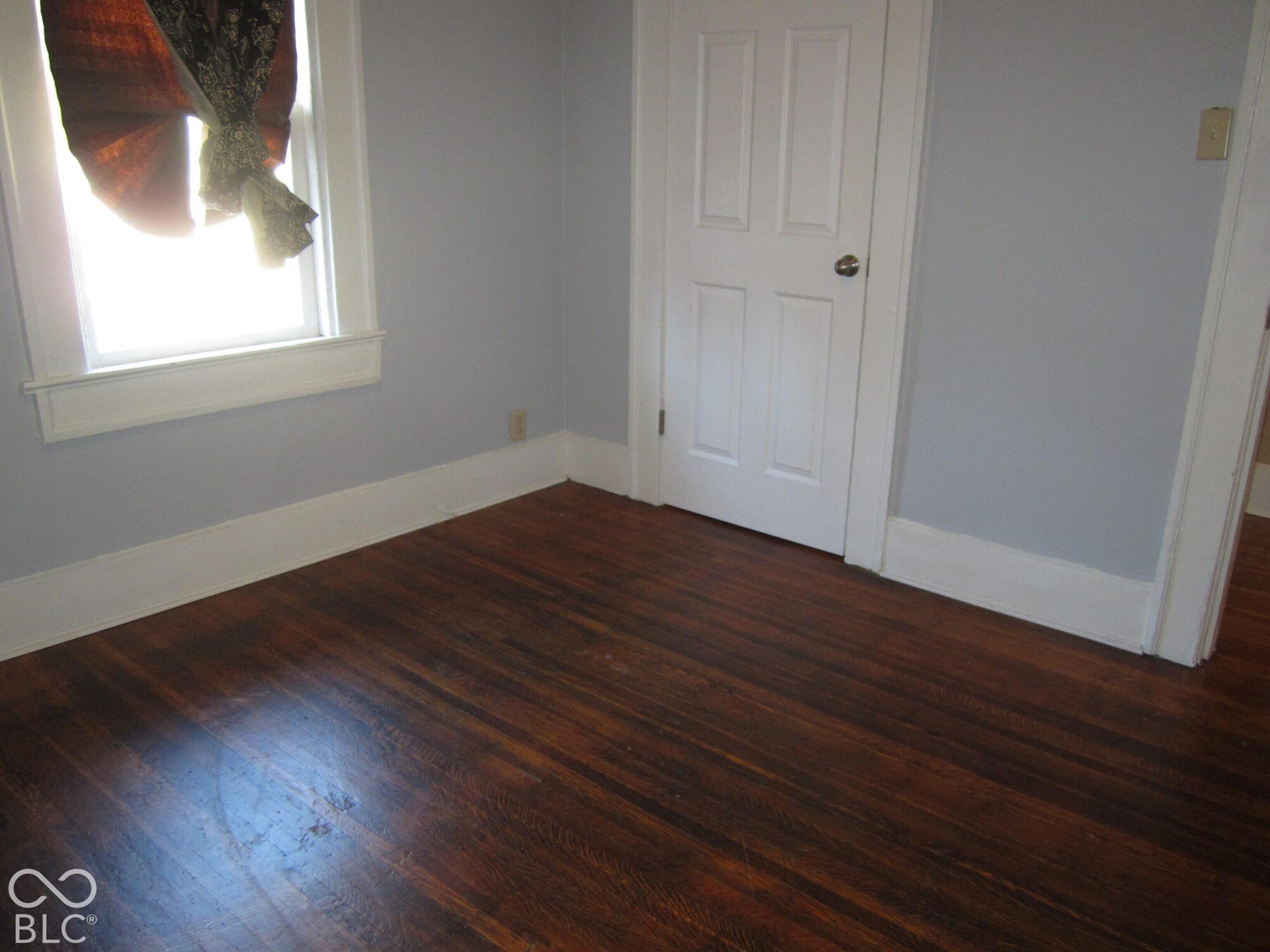 Interior room featuring dark-stained wood-finish flooring, white four-panel door, and window with white casing