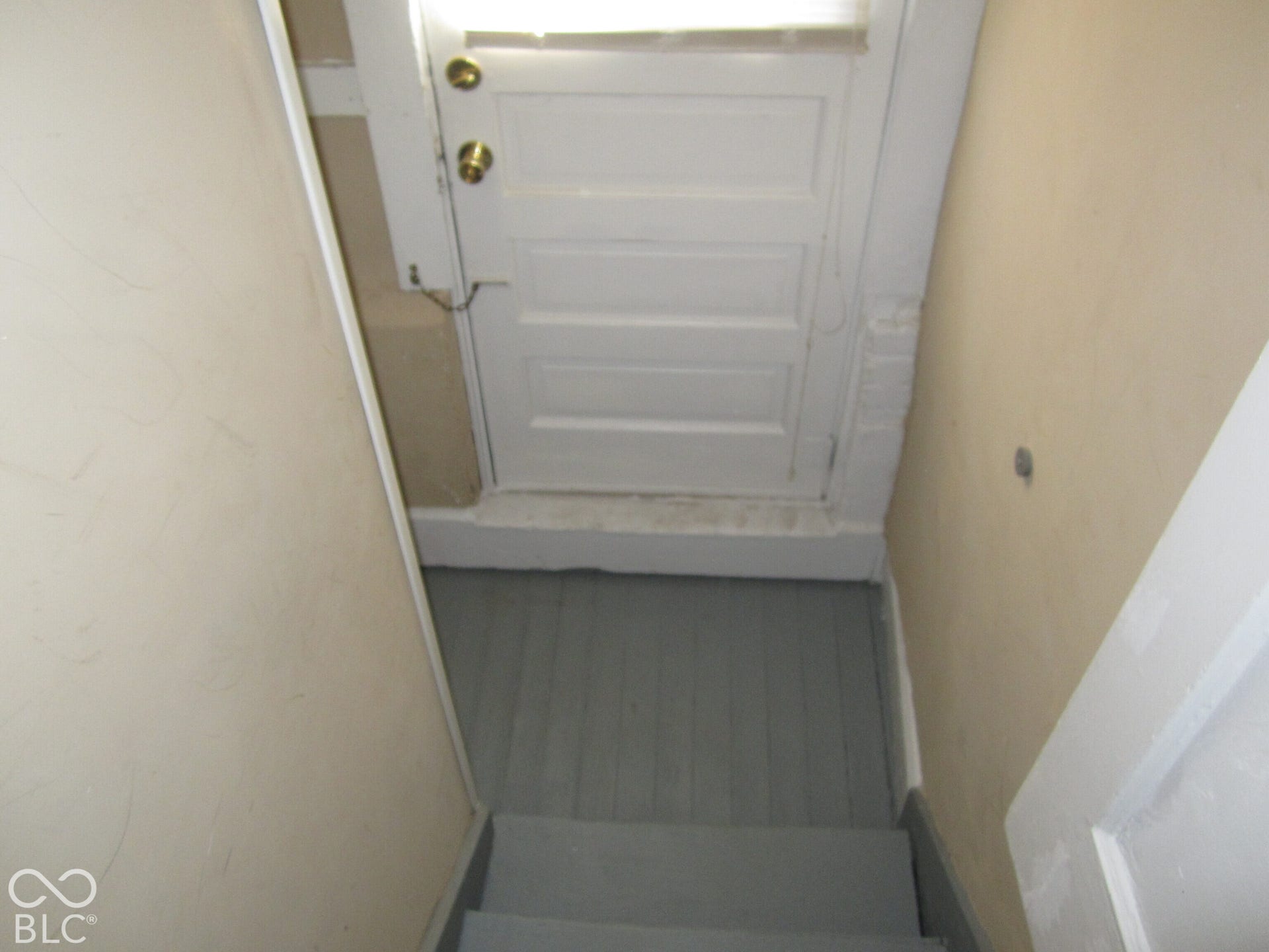 Painted wooden staircase featuring a white paneled door with brass-finish hardware