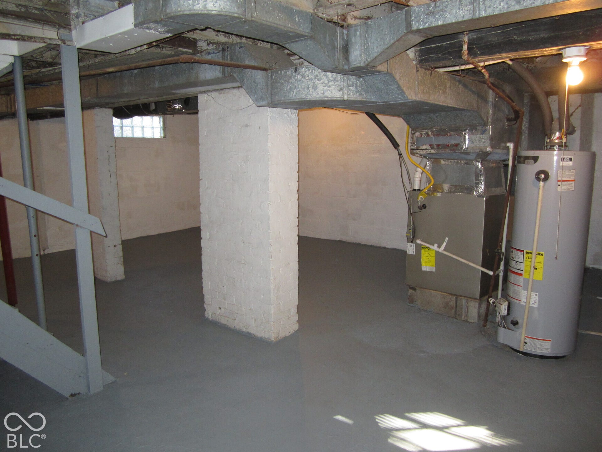 Unfinished lower level featuring painted concrete flooring, structural masonry support pillars, exposed metal ductwork, a vertical furnace, and a water heater
