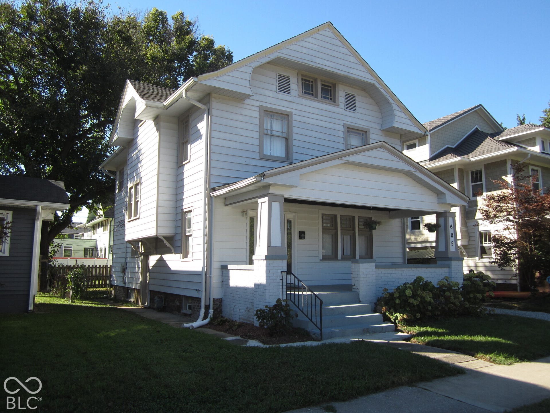 Two-story exterior featuring white horizontal siding, a covered front porch with brick pillars, and a decorative gable pediment