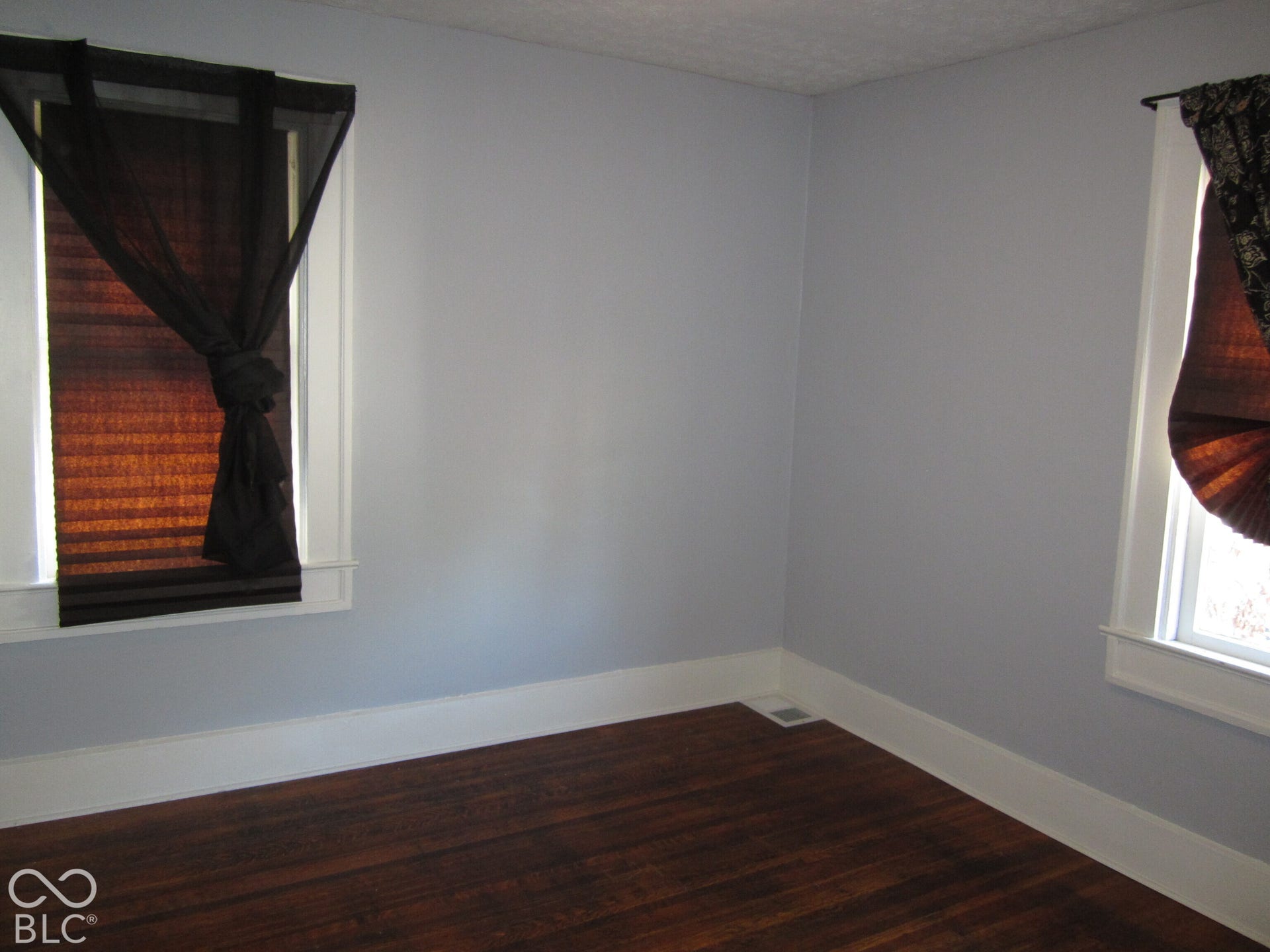 Room featuring wood-finish flooring and two windows with white trim