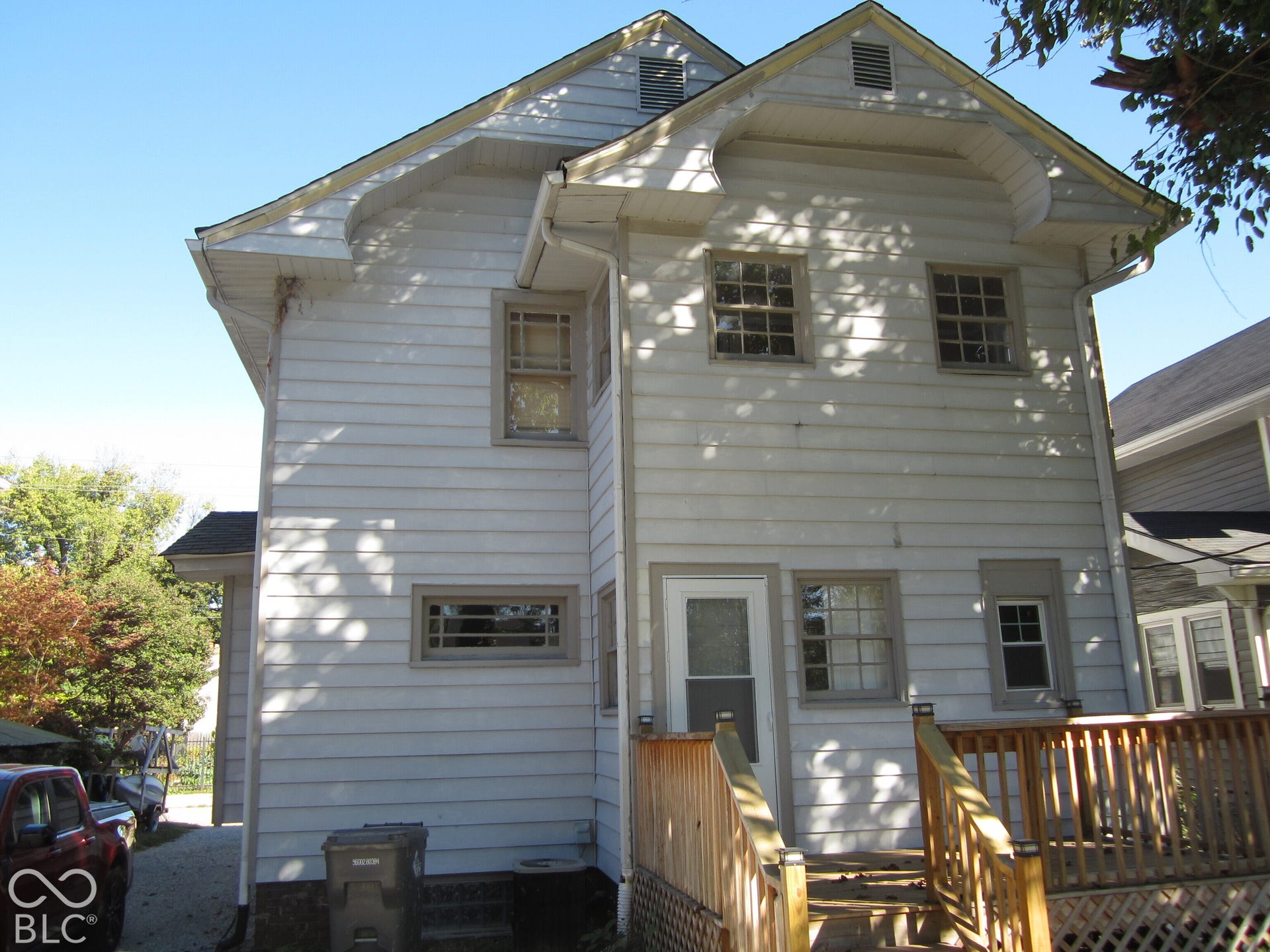 Two-story home exterior featuring white horizontal siding, a gabled roofline, multi-pane windows, and a wood-deck platform