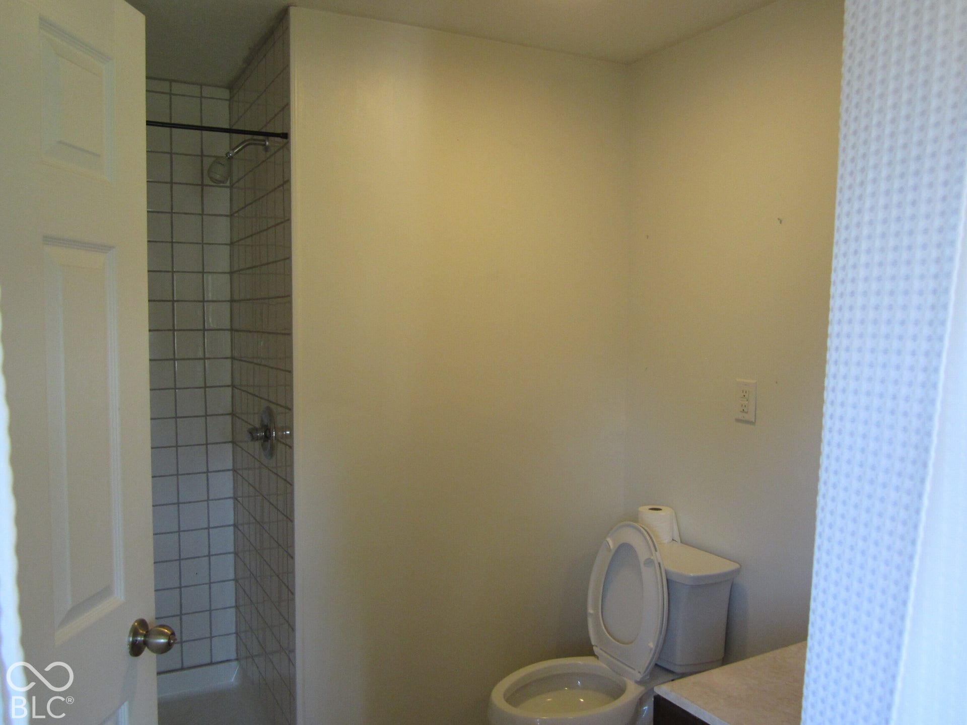 Bathroom featuring a walk-in shower with white grid-patterned wall tile, a standard-profile toilet, and a vanity with a solid-surface countertop