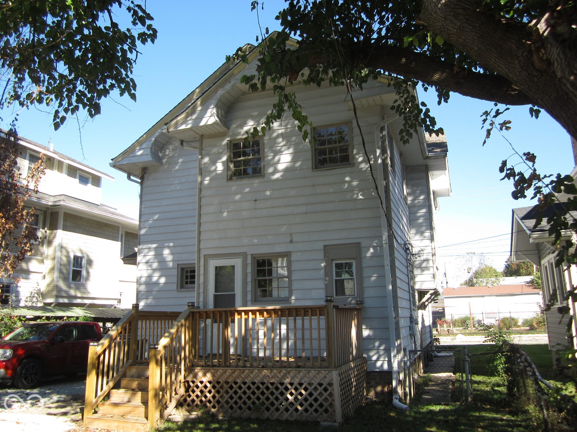 Two-story exterior featuring white horizontal siding, a wood-framed deck with lattice skirting, a gable roof, and multiple multi-pane windows