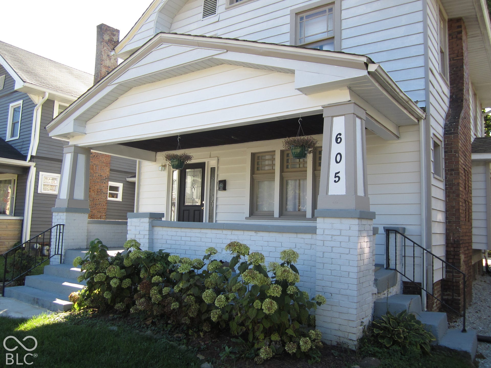 Covered front porch featuring tapered support columns, painted brick base, and side stairs with iron railings