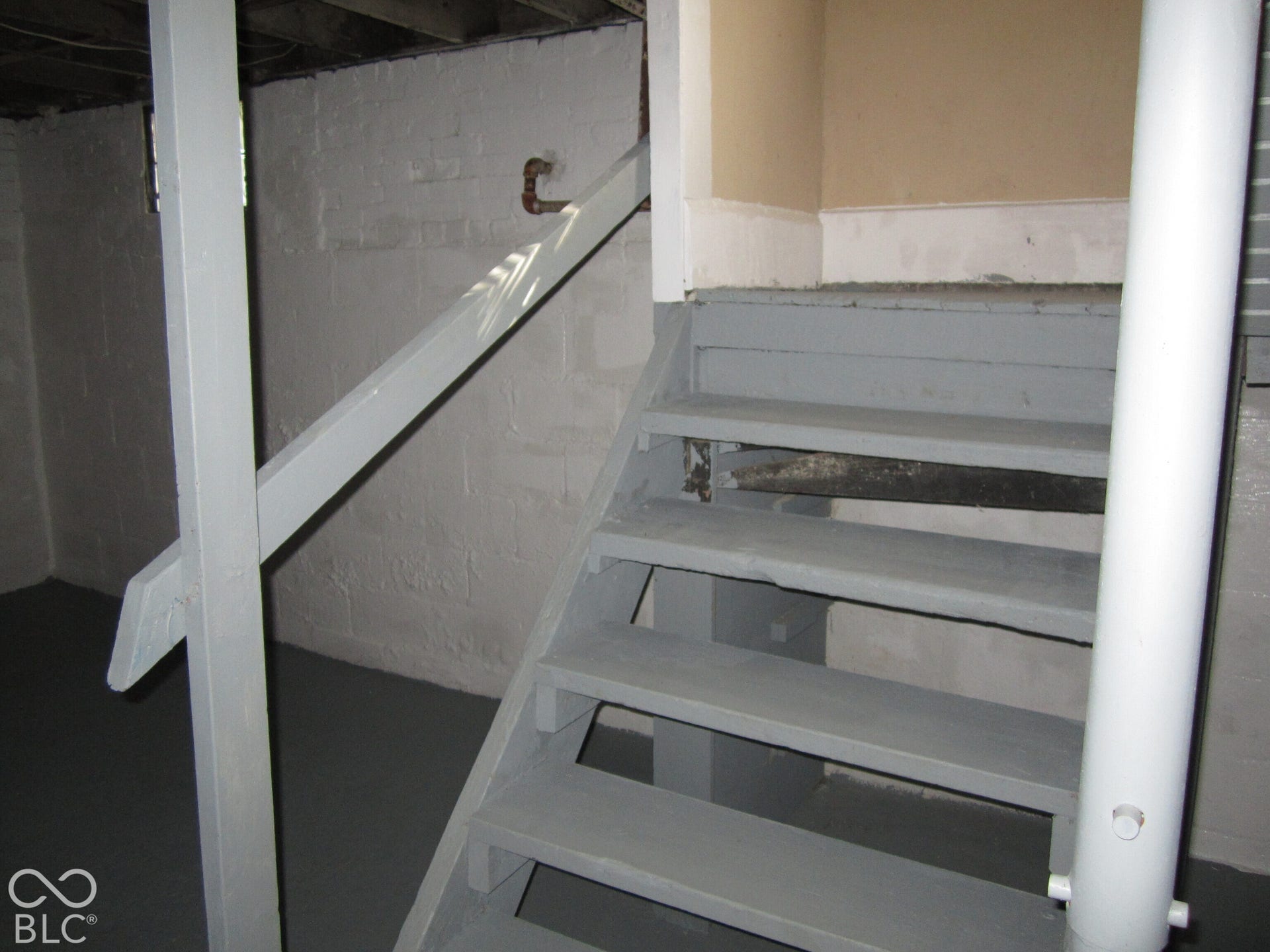 Painted concrete block walls, gray-finished timber staircase with a single handrail, and structural steel support columns