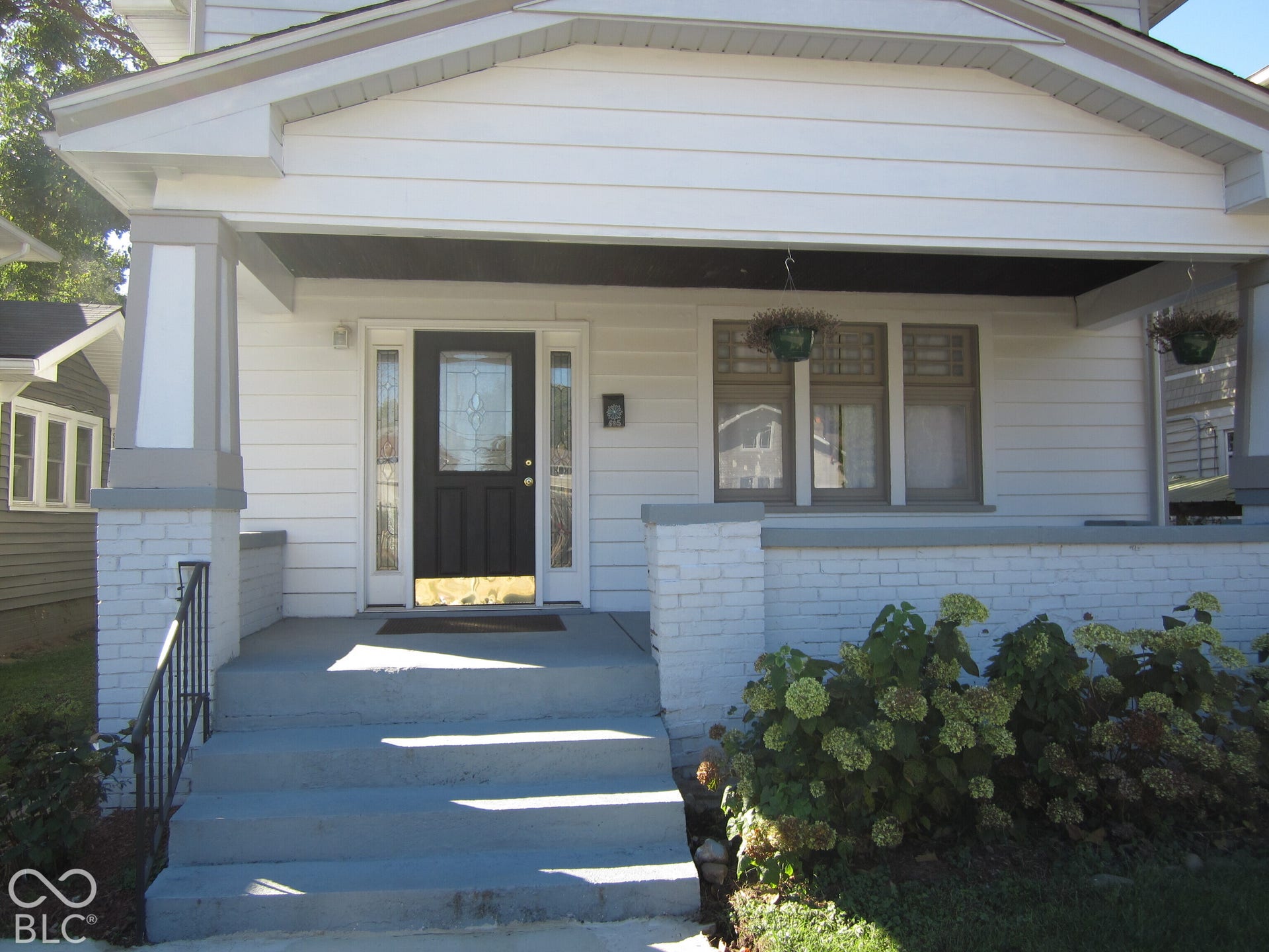 Covered front porch featuring white painted brick pillars, horizontal siding, black front door with decorative glass inlay, and flanking sidelights