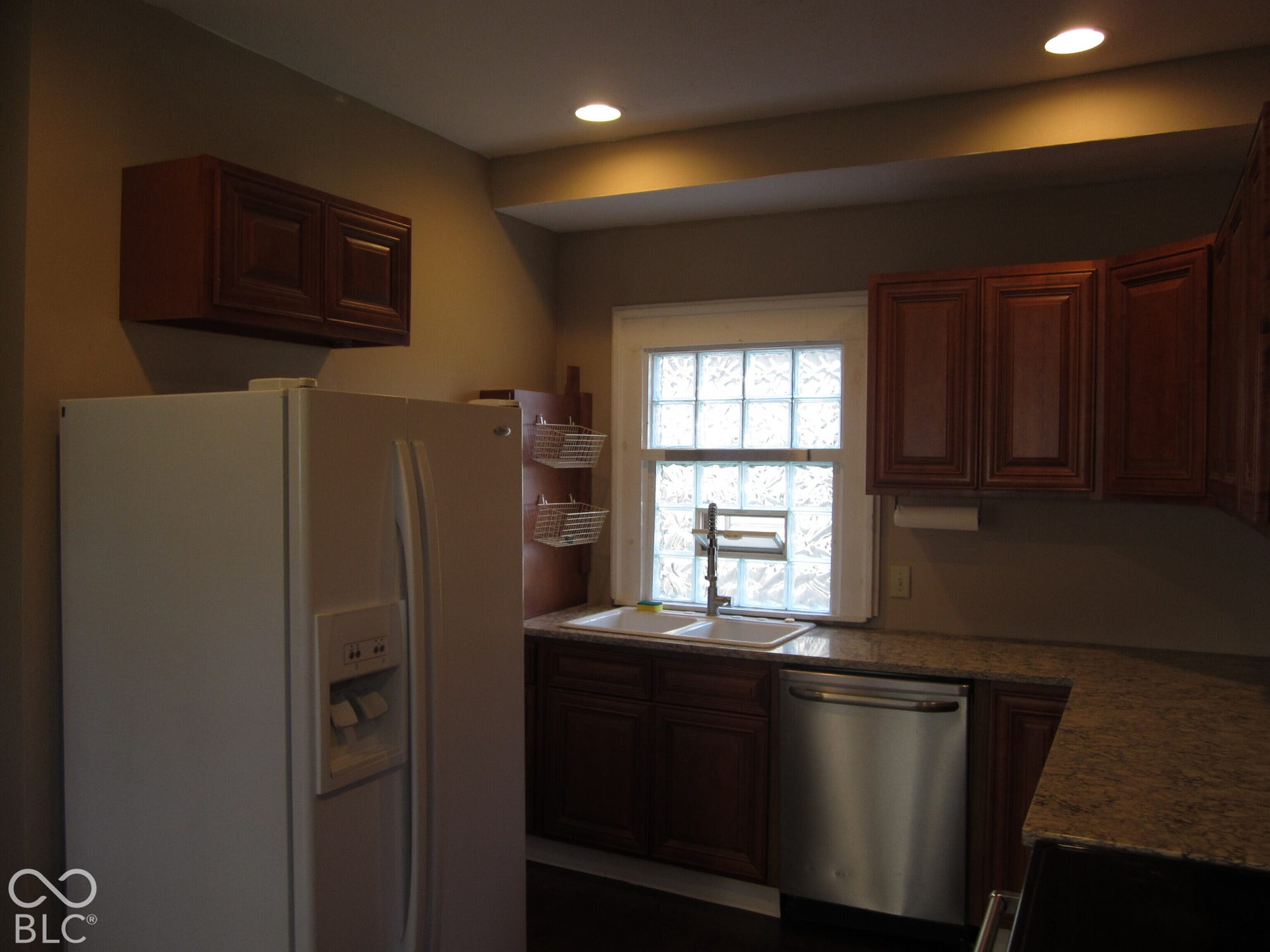 Kitchen featuring dark wood-finish cabinetry, stone-finish countertops, dual-basin sink, stainless steel dishwasher, and recessed lighting