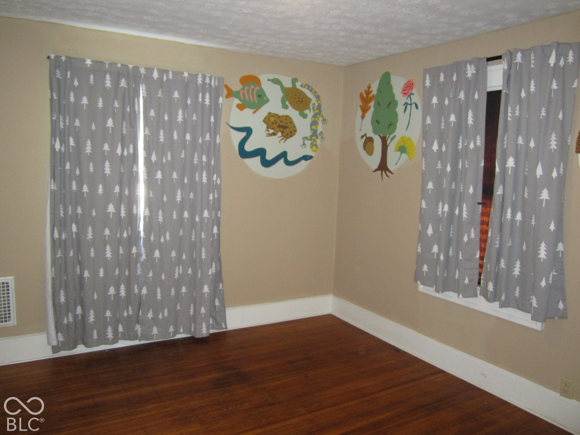 Interior room featuring polished wood-finish flooring, two windows with white trim, and neutral wall paint