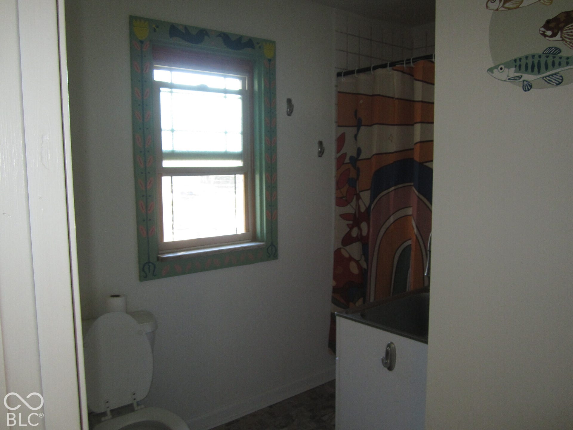 Single-hung window with decorative painted trim, wall-mounted hardware, and tiled tub enclosure