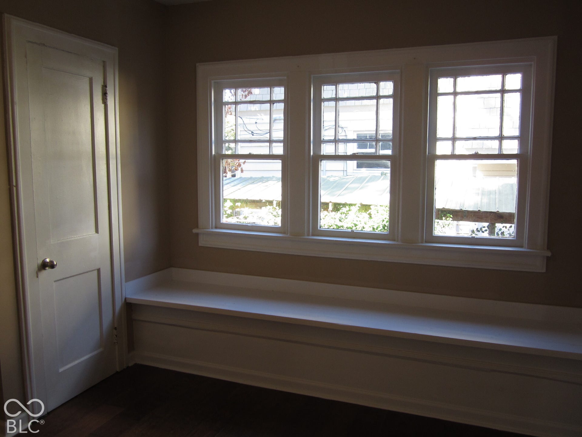 Built-in window bench with white millwork, triple-pane divided-light windows, and a single-panel interior door with brushed metal hardware