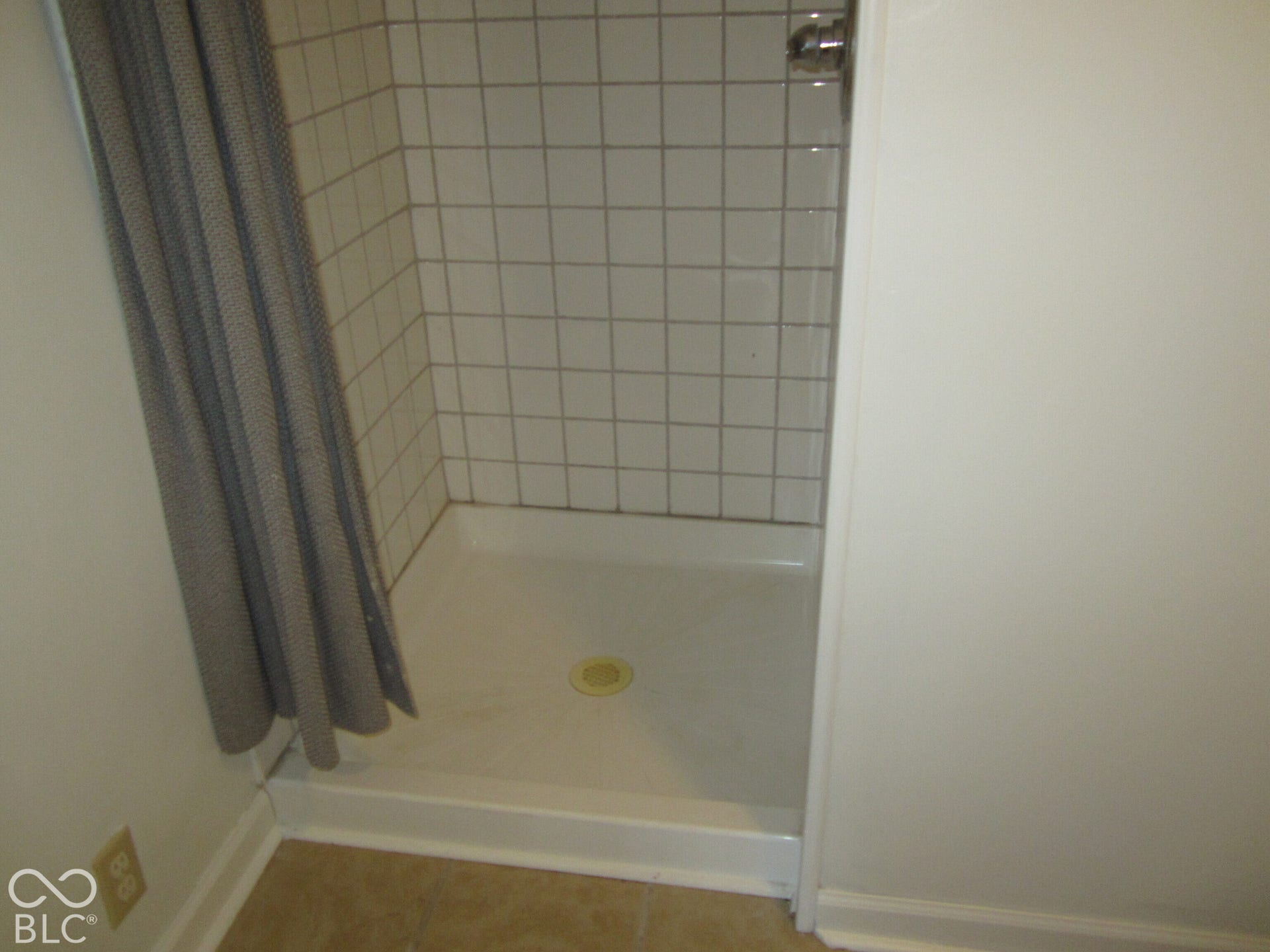 Walk-in shower stall featuring square wall tile, a white acrylic basin, and metal faucet hardware