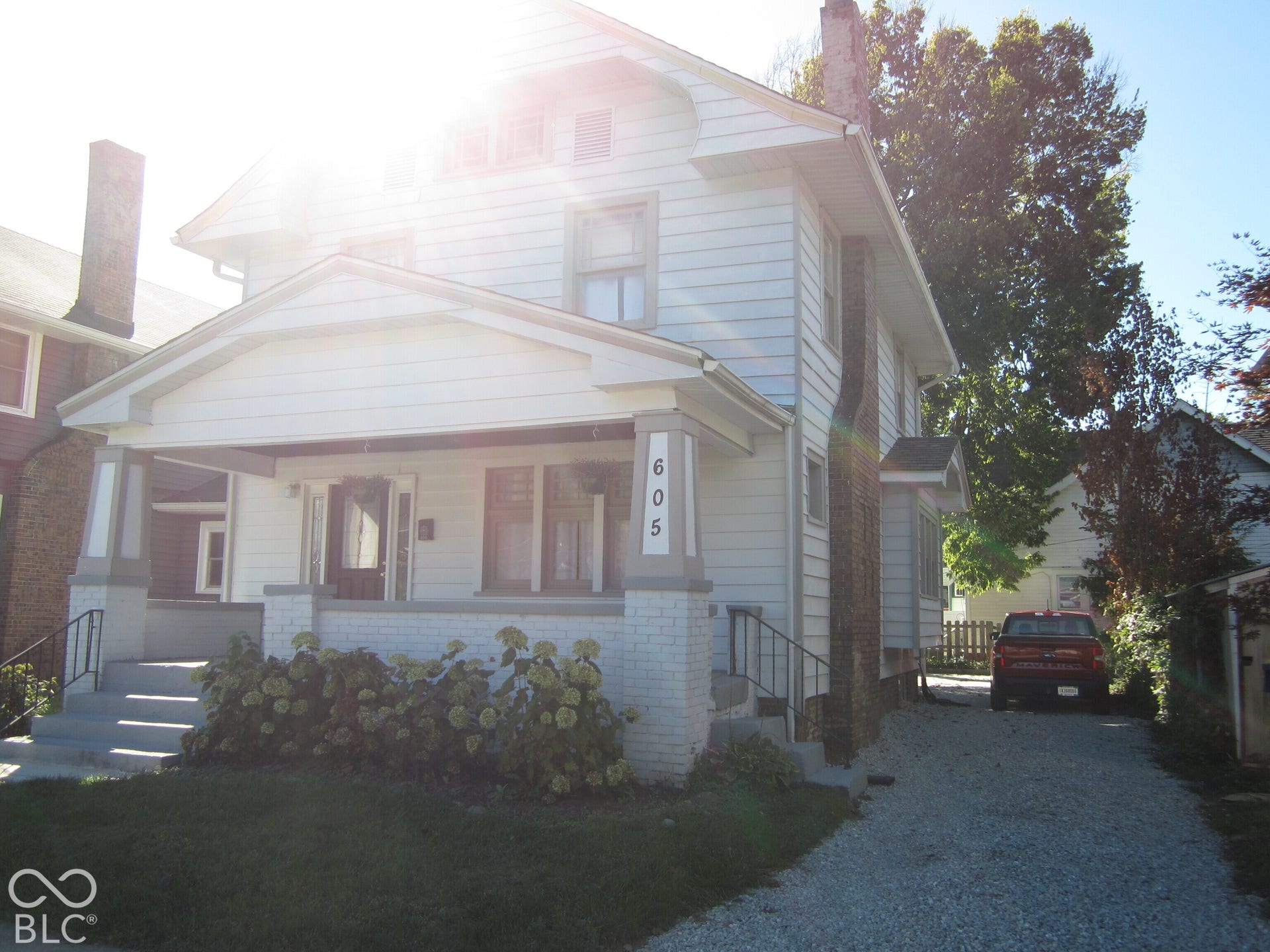Two-story exterior featuring white horizontal siding, a covered front porch with brick column bases, and a stone driveway