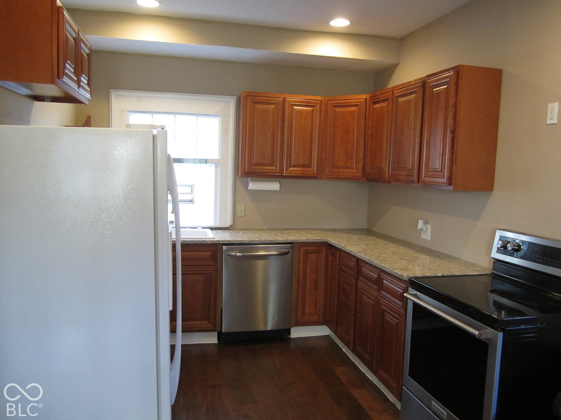 Kitchen featuring wood-finish cabinetry, stone-surfaced countertops, stainless steel dishwasher, integrated electric range, and wood-finish flooring