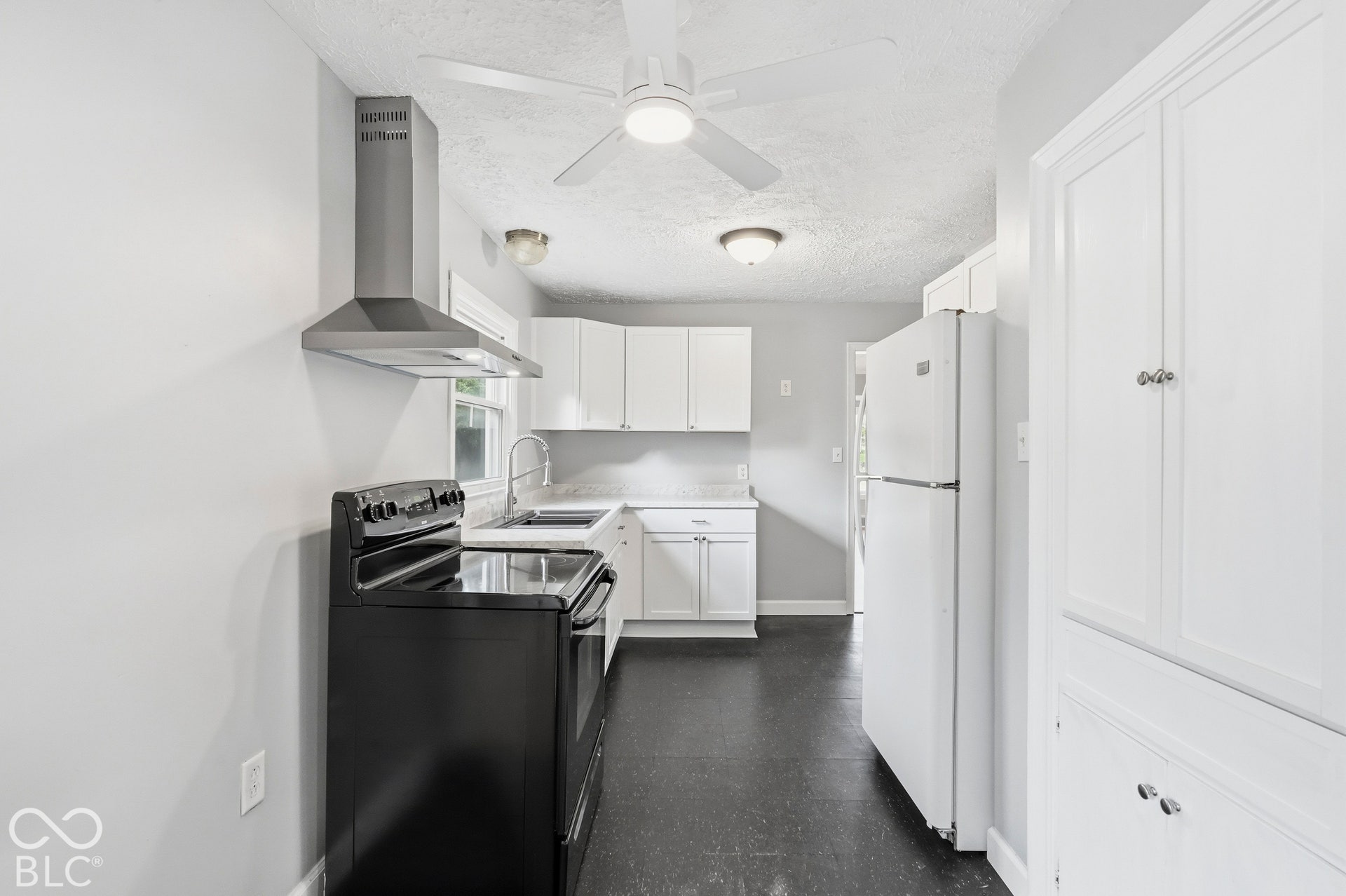 Kitchen featuring white cabinetry, stainless steel range hood, dark flooring, built-in pantry storage, and a ceiling-mounted light fixture