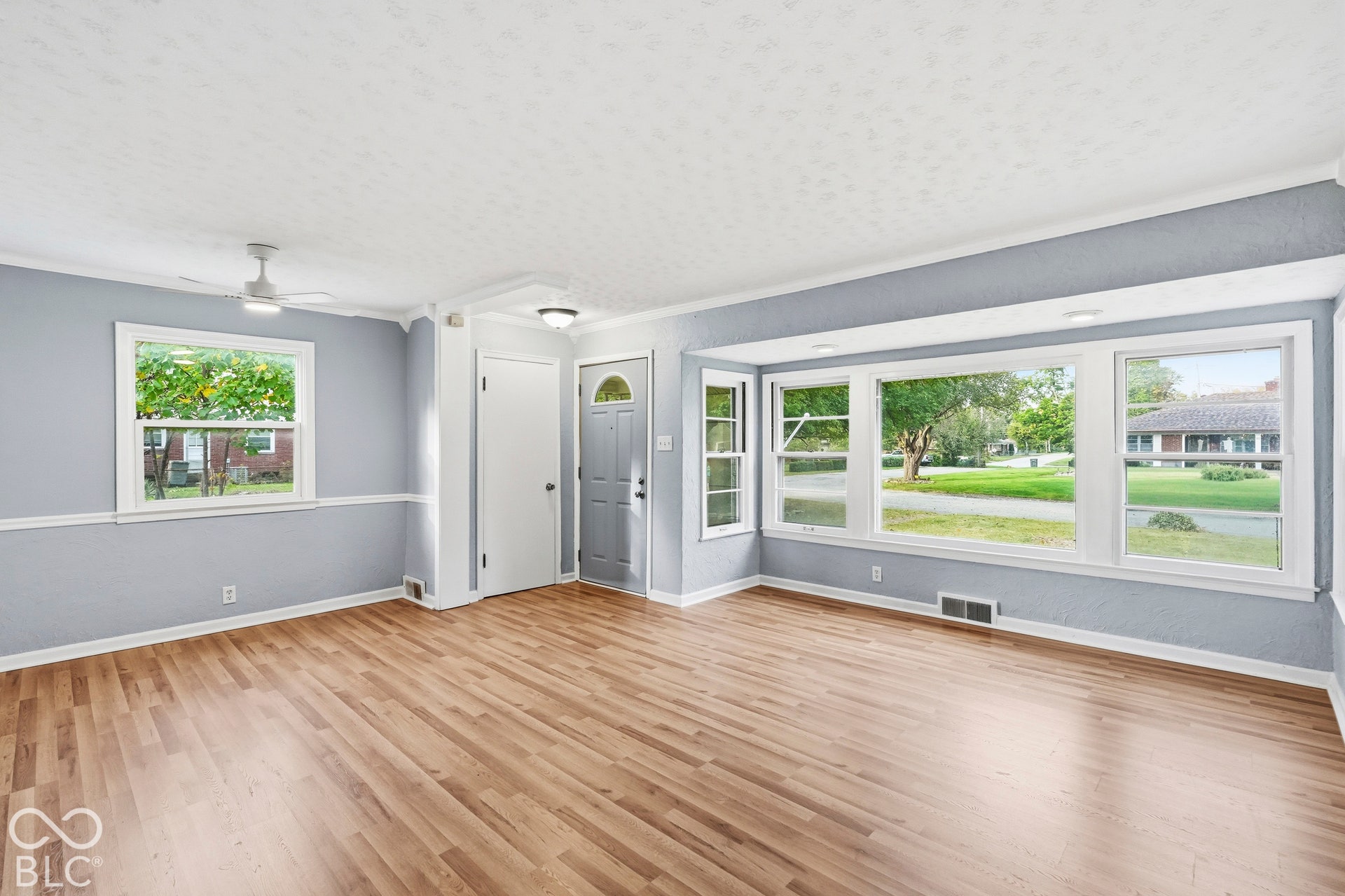 Living area featuring wood-finish flooring, a tripartite picture window, crown molding, and a ceiling fan with integrated lighting