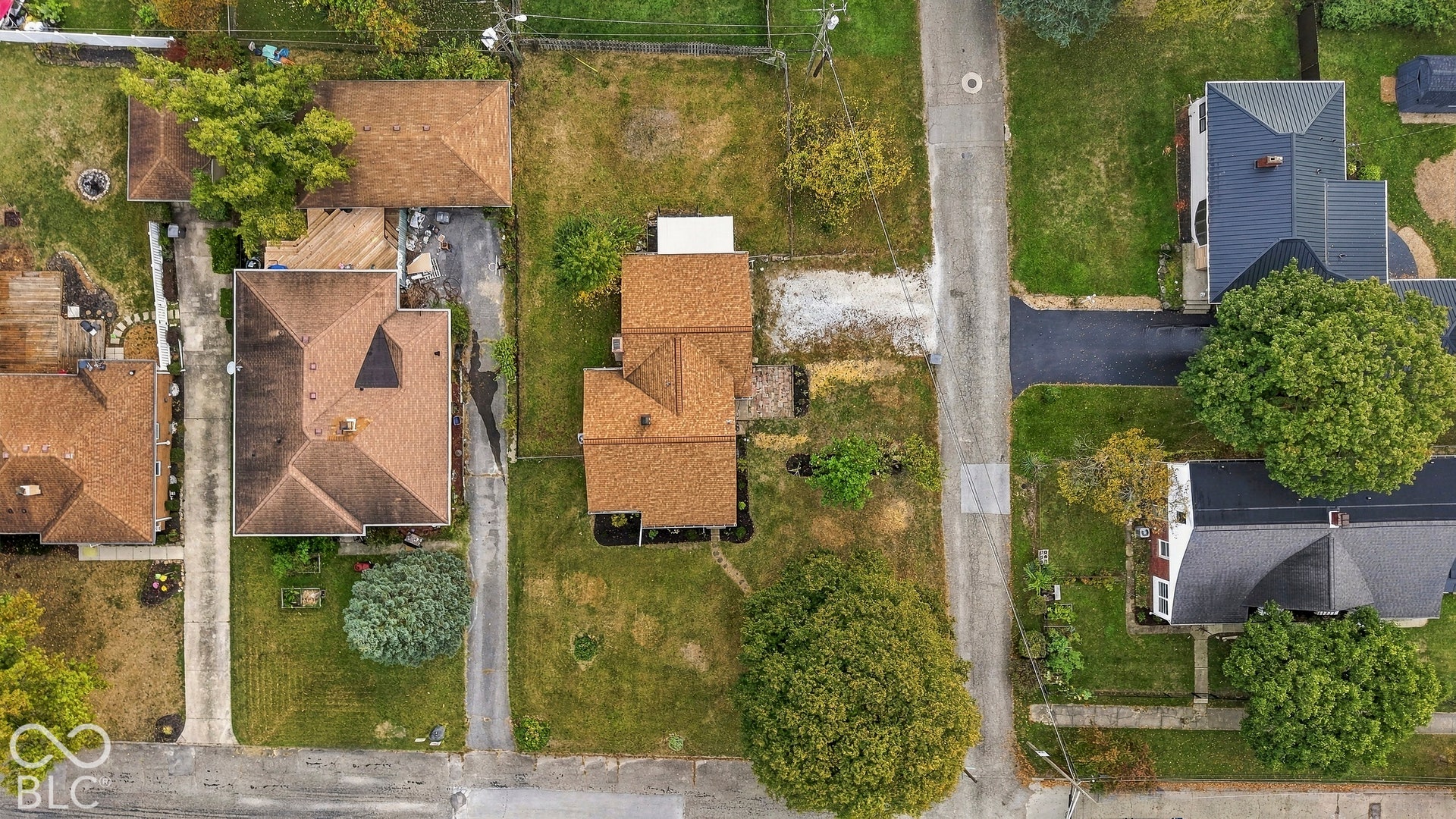 Aerial perspective of residential lot featuring mature trees, grass lawn, asphalt driveway, and shingle-roof structure