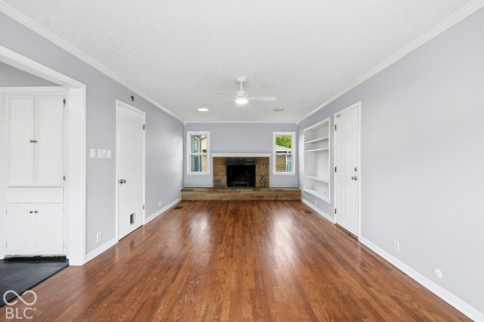 Wood-finish flooring, masonry fireplace with a raised stone hearth, built-in shelving, and a ceiling-mounted light fixture