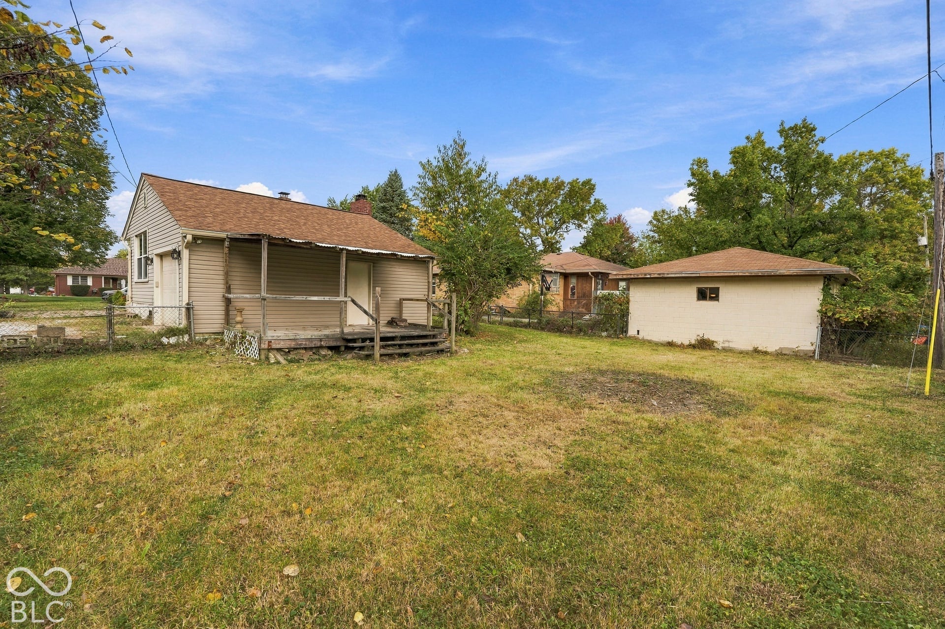 Expansive backyard featuring a detached garage, elevated wooden deck, chain-link fencing, and mature trees