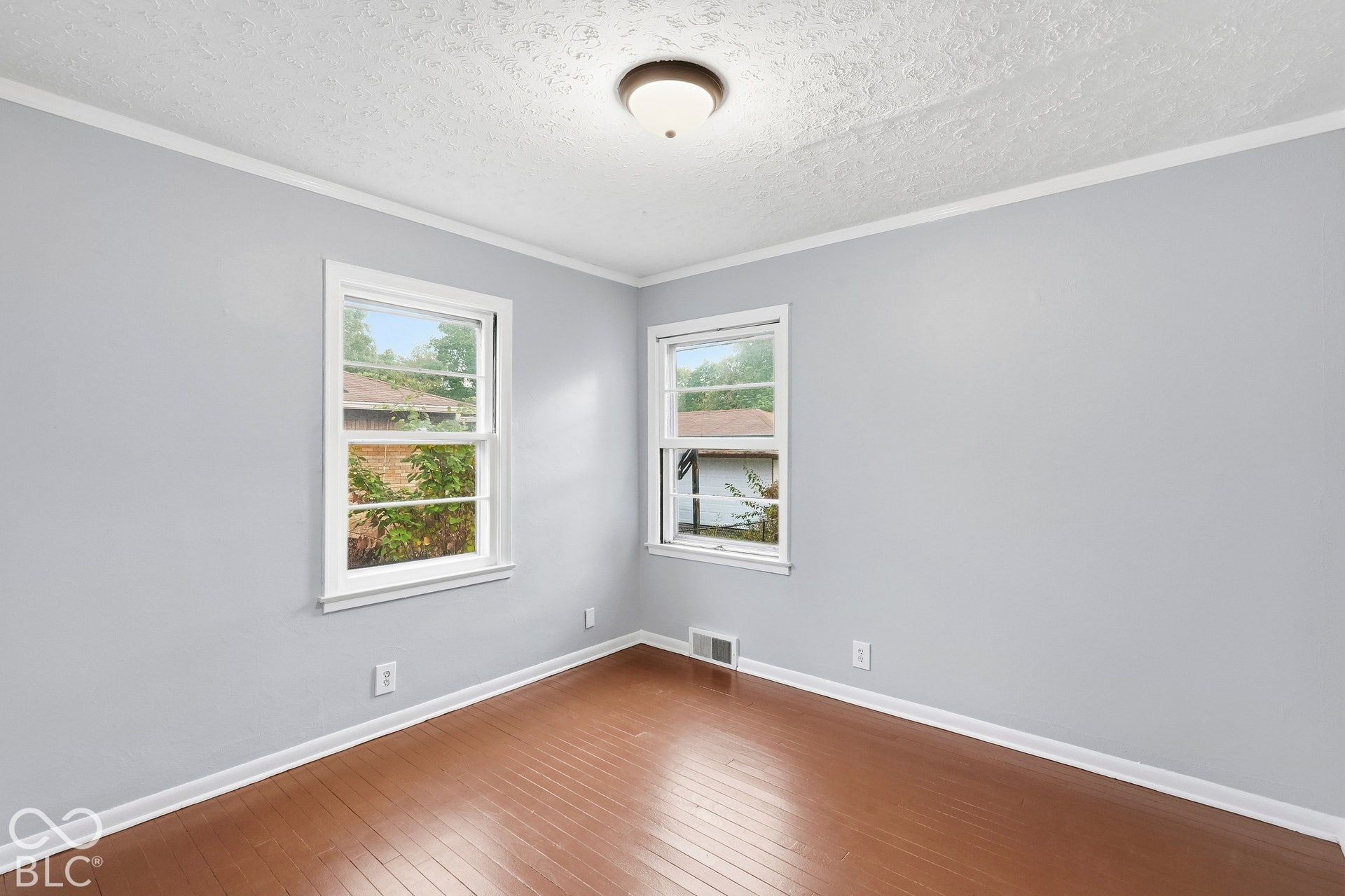 Neutral-toned interior room featuring wood-finish flooring, dual windows with white trim, and a flush-mount ceiling light fixture