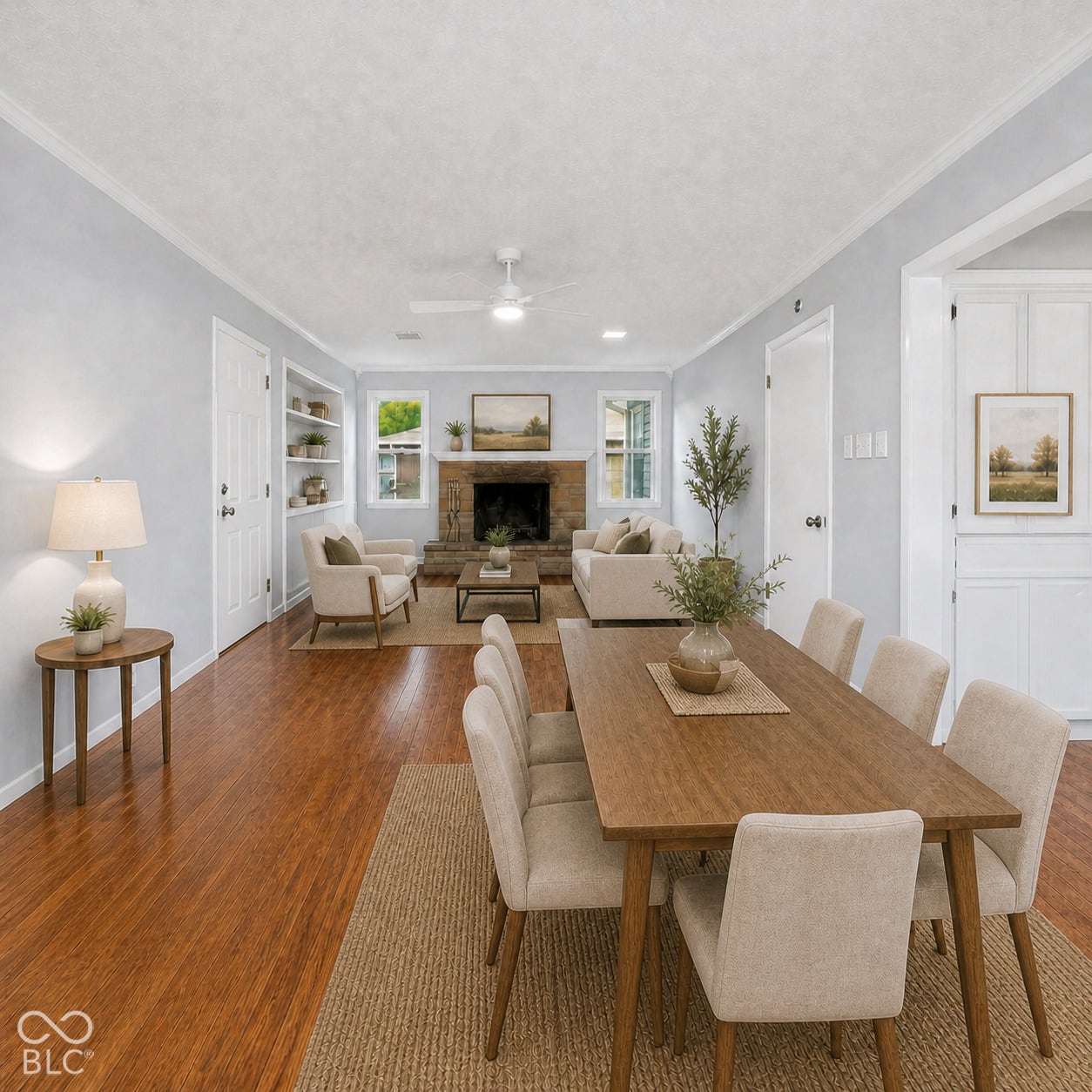 Living area featuring wood-finish flooring, stone fireplace, built-in shelving, crown molding, and white ceiling fan. Virtually altered.