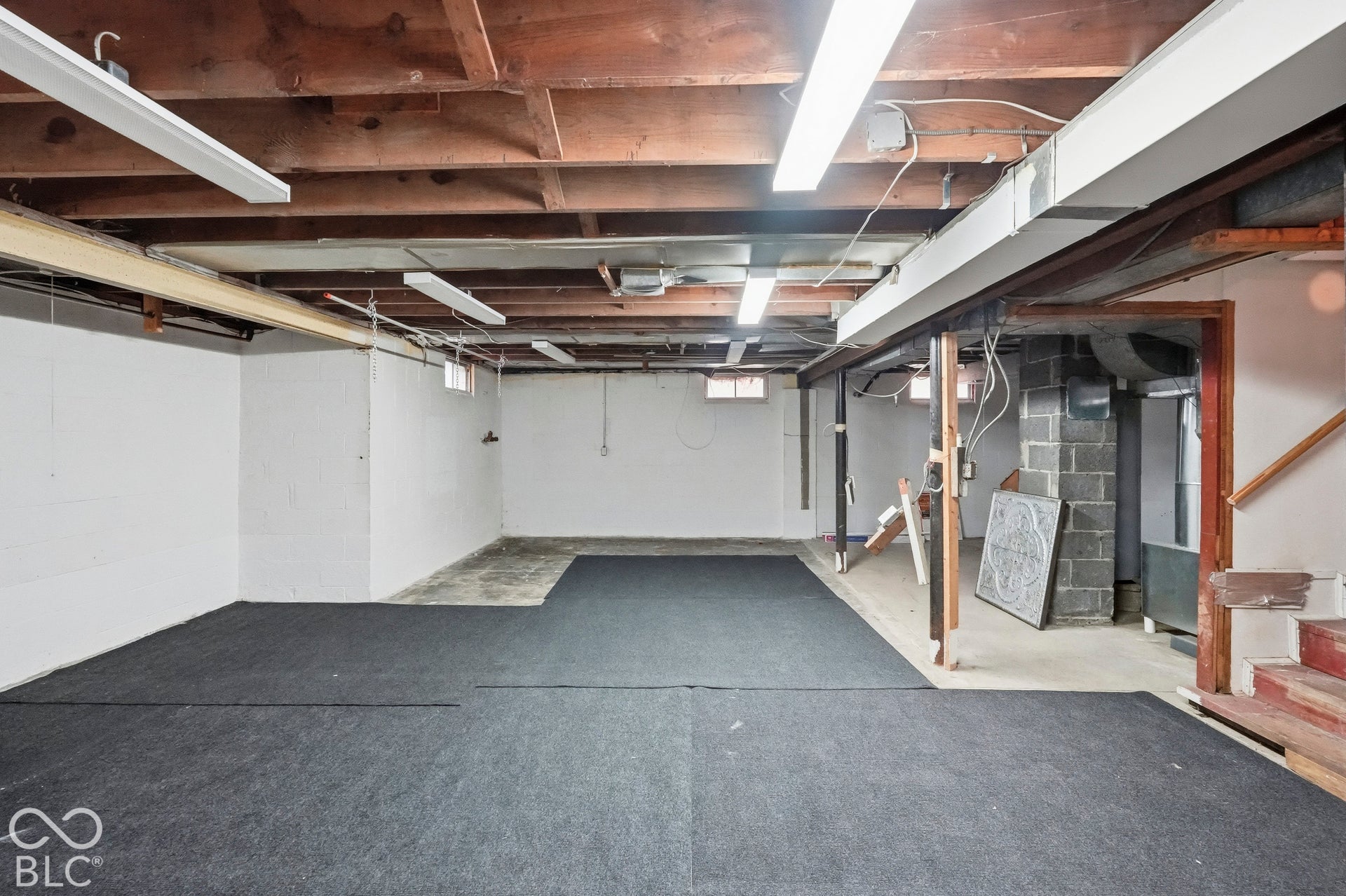 Unfinished space featuring exposed timber joist ceiling, concrete floor, white painted walls, and linear fluorescent lighting