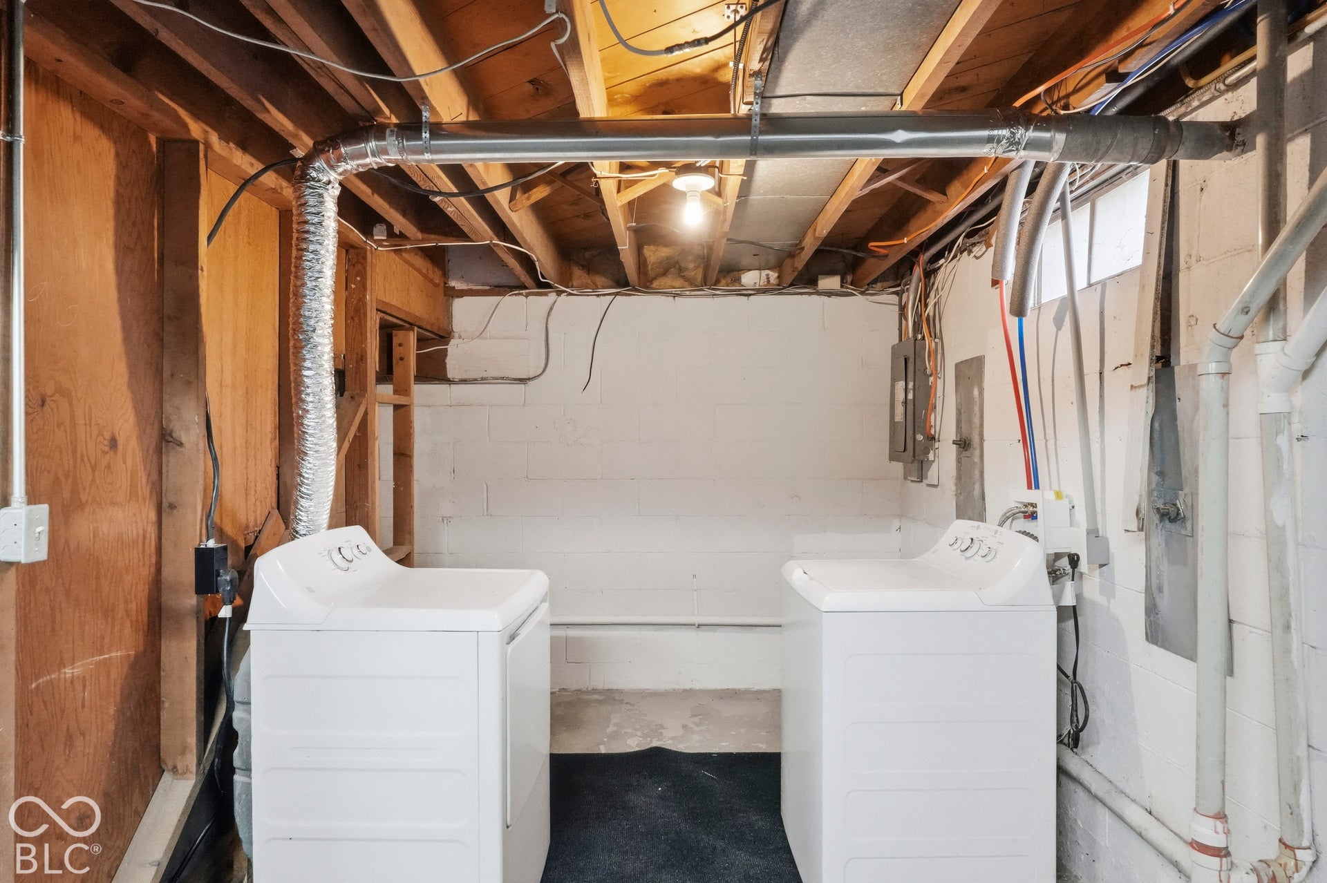 Utility area featuring painted concrete block walls, exposed wood ceiling joists, metal ductwork, and dedicated plumbing connections