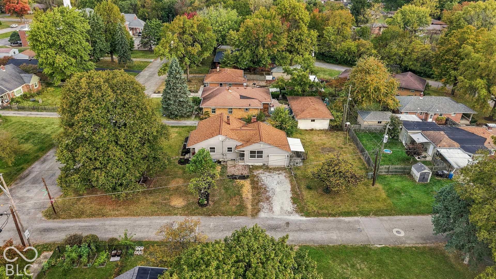 Single-story residence featuring a shingled roof, light-colored exterior siding, and an attached garage situated on an expansive lot with mature trees