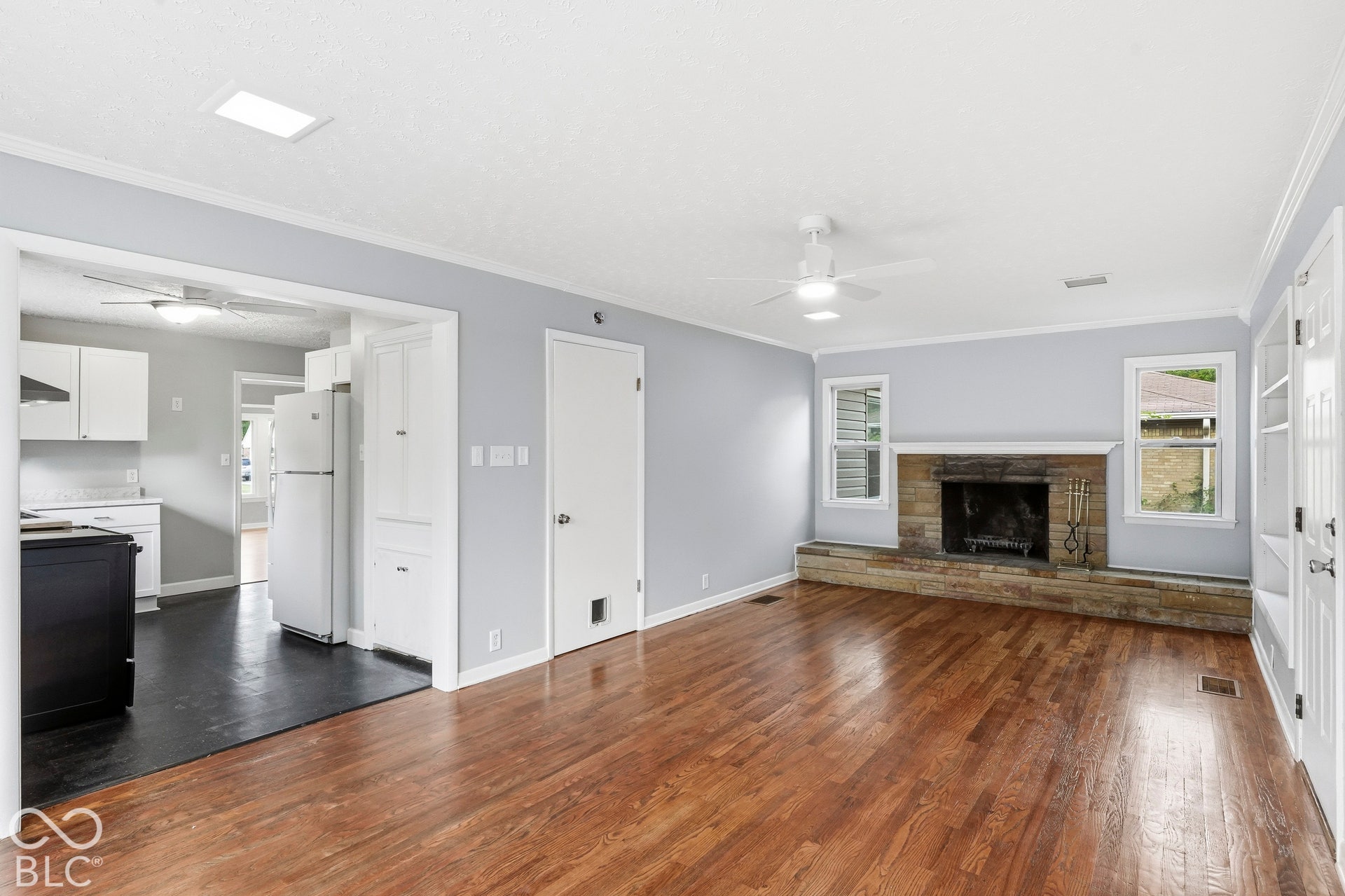 Living area featuring wood-finish flooring, a masonry fireplace with an extended stone hearth, recessed ceiling lighting, and built-in shelving