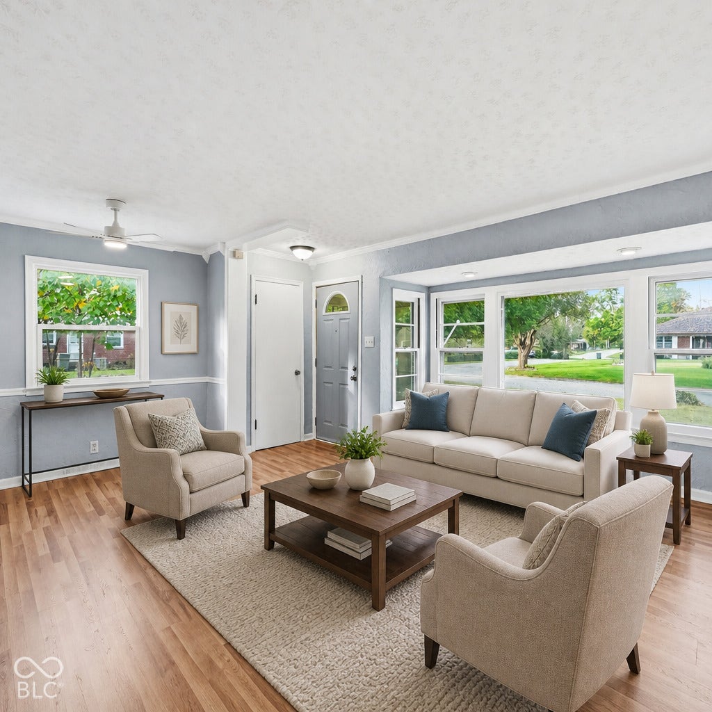 Living area featuring wood-finish flooring, a large bay window, ceiling-mounted light fixtures, and chair rail molding. Virtually altered.