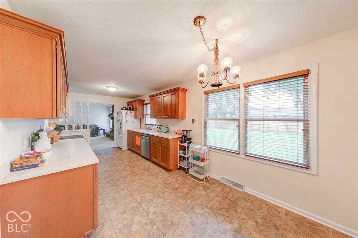 Kitchen featuring wood cabinetry, solid-surface countertops, tile flooring, and a multi-light chandelier
