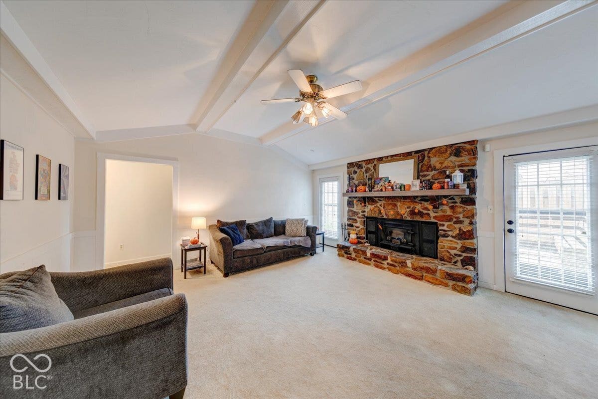 Vaulted ceiling with exposed structural beams, floor-to-ceiling stone fireplace, masonry hearth, and glass-paneled exterior door