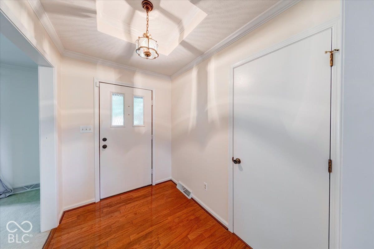 Entryway featuring wood-finish flooring, a recessed tray ceiling, crown molding, and a decorative pendant light fixture