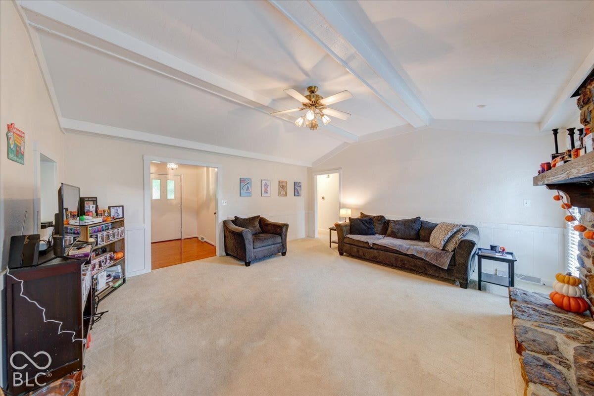 Vaulted ceiling featuring exposed beams, stone fireplace surround, and a ceiling-mounted light fixture