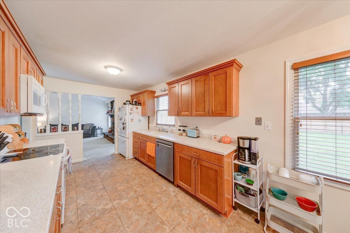 Kitchen featuring wood cabinetry, laminate countertops, tiled flooring, built-in stainless steel appliances, and a window with blinds