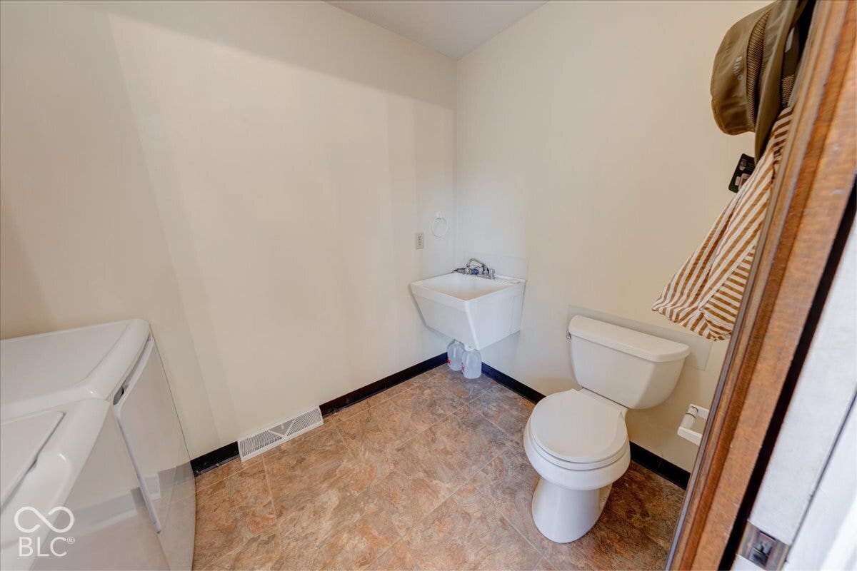 Utility space featuring a wall-mounted basin, porcelain toilet, and resilient patterned flooring