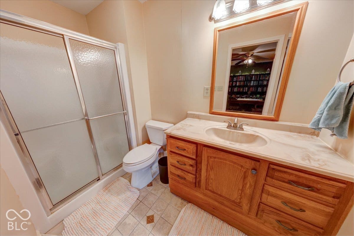 Bathroom featuring a wood vanity with a solid surface countertop, integrated sink, large wall-mounted mirror, and a walk-in shower with a sliding glass enclosure
