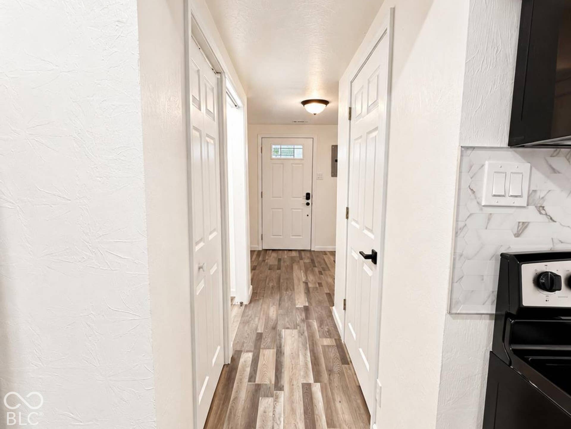 Hallway featuring wood-finish flooring, white panel doors with matte black hardware, and an exterior door with a decorative glass insert