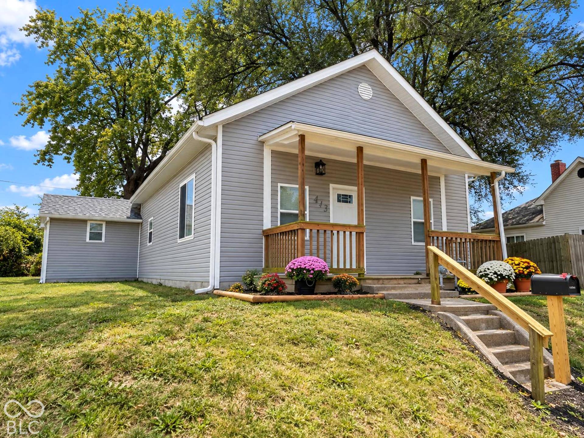 Gray siding exterior featuring a covered front porch with wood-finish railings, asphalt shingle roofing, and concrete steps with a wood-finish handrail