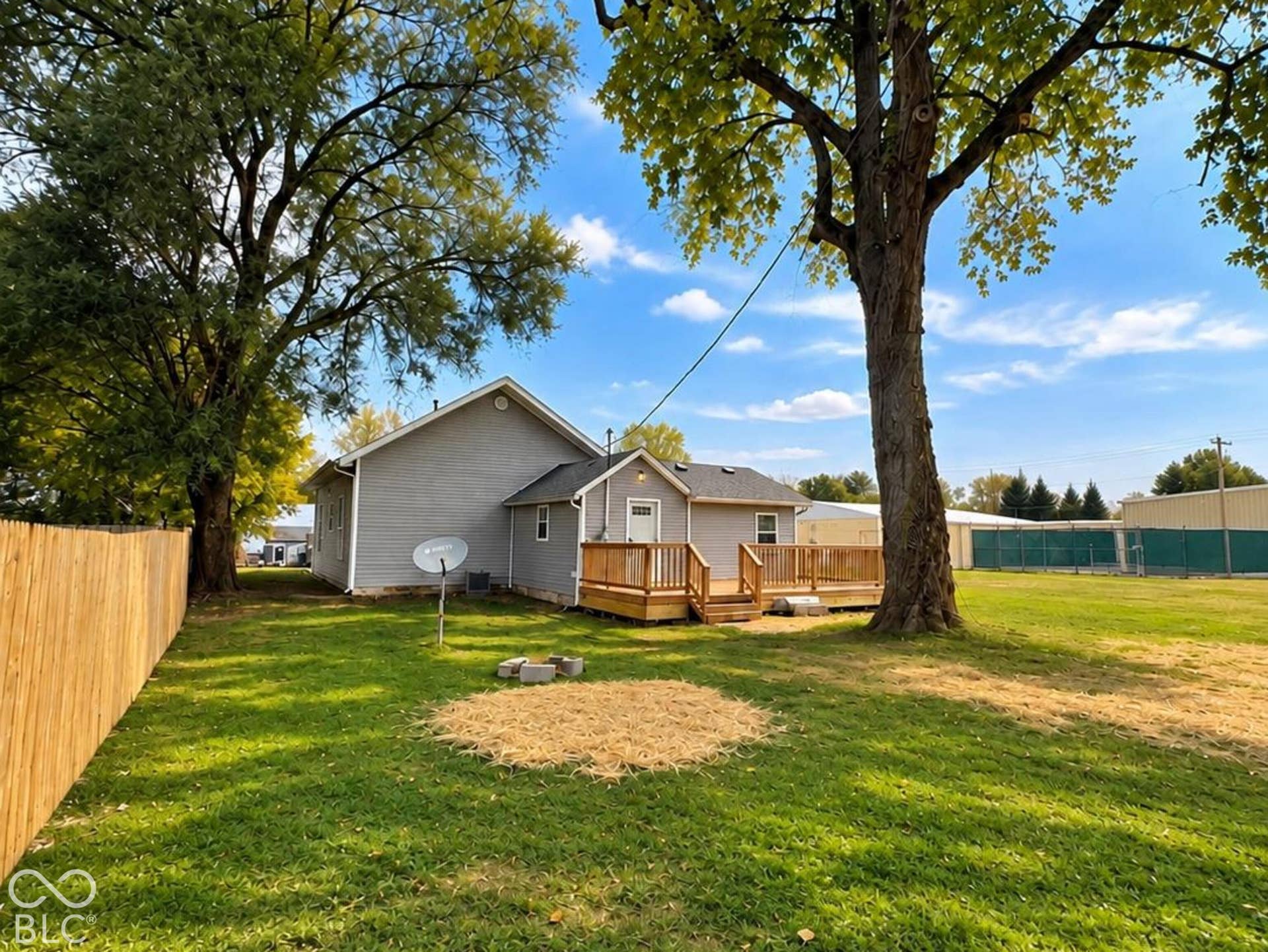 Expansive backyard featuring a wood deck, mature trees, wood privacy fencing, and exterior siding