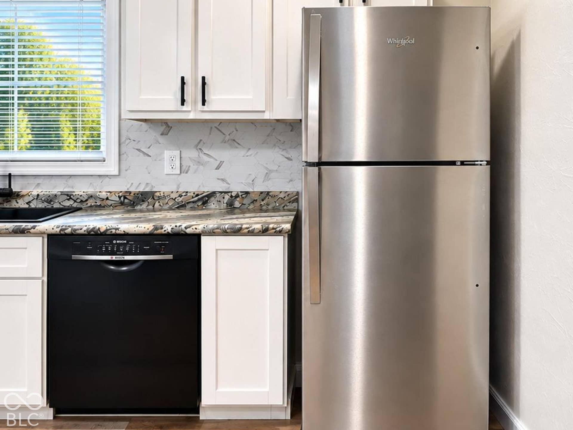 Kitchen featuring white cabinetry, stone-patterned countertops, stainless steel refrigerator, black dishwasher, and black faucet