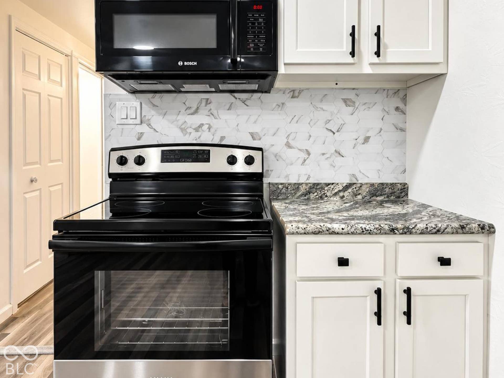 Kitchen featuring white Shaker-style cabinetry with matte black hardware, stone-finish countertops, tiled backsplash, and stainless steel and black appliances